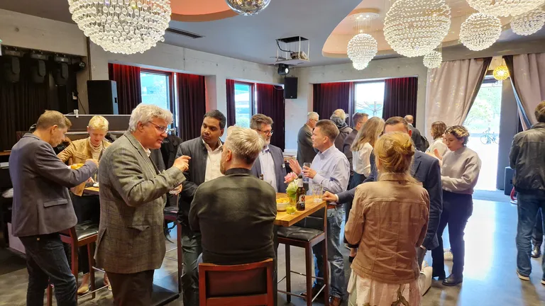 Leute stehen in einer Bar an Stehtischen und unterhalten sich.
