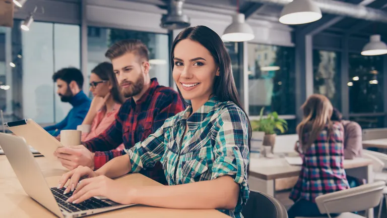Zwei Frauen und zwei Männer sitzen nebeneinander an einem Tisch und schauen auf Laptops und Tablets