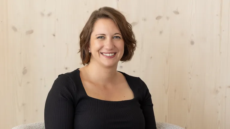 Elise Bourgeois, Gründerin der Agentur onyva lächelt vor einem hellen Holzhintergrund in die Kamera.
