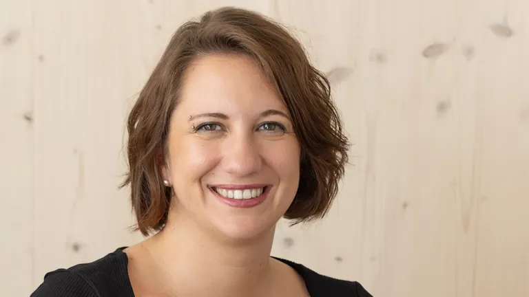 Elise Bourgeois, Gründerin der Agentur onyva lächelt vor einem hellen Holzhintergrund in die Kamera.