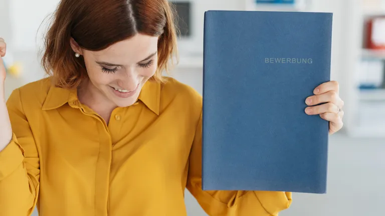 Young woman in a yellow blouse holds a job application folder in her hand and is happy.