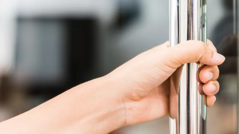 Eine Hand hält die Metallstange fest, die an einer gläsernen Tür angebracht ist. Auf dem Glas rechts von der Stange steht pull in Grossbuchstaben.